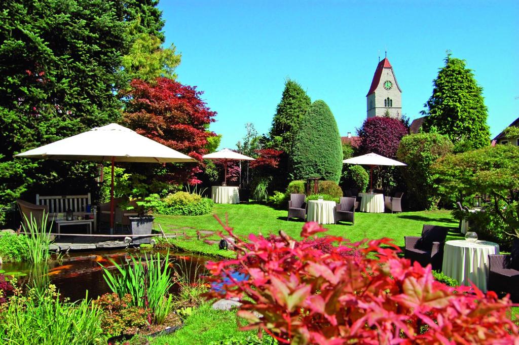 einen Garten mit einem Teich und einem Uhrturm in der Unterkunft Hotel Der Löwen in Hagnau