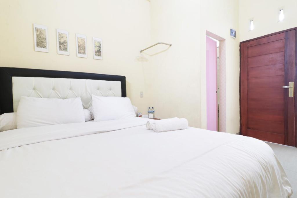 Cama blanca con sábanas blancas y puerta marrón en Krisna Hostel, en Medan
