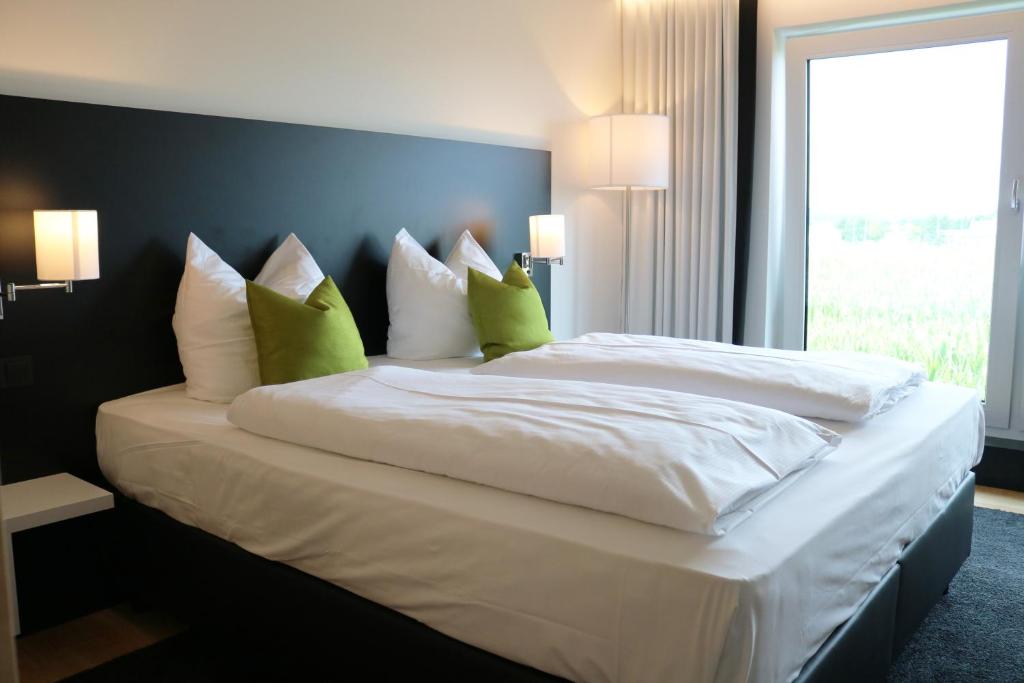 uma cama grande com lençóis brancos e almofadas verdes em NU Hotel by WMM Hotels em Neu-Ulm