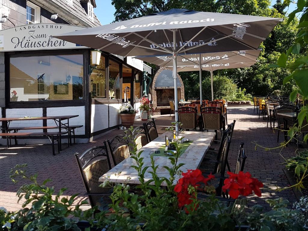 un patio con mesas, sillas y una sombrilla en Landgasthof Zum Häuschen en Rösrath