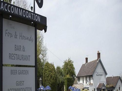 um sinal para um bar e restaurante ao lado de uma casa em The Fox & Hounds em Swindon