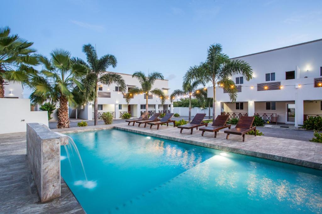 a pool with chairs and palm trees in front of a building at Curadise Living in Willemstad