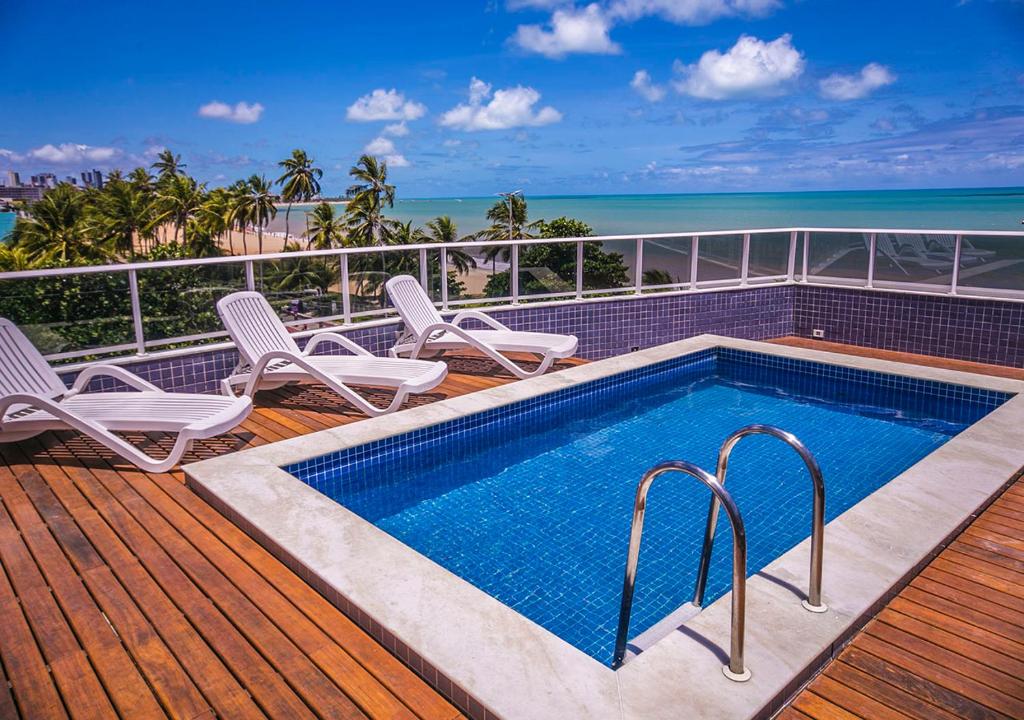 una piscina en una terraza con sillas y el océano en ATLANTICO SUL Flat - Cabo Branco by PenareiaTurBr, en João Pessoa