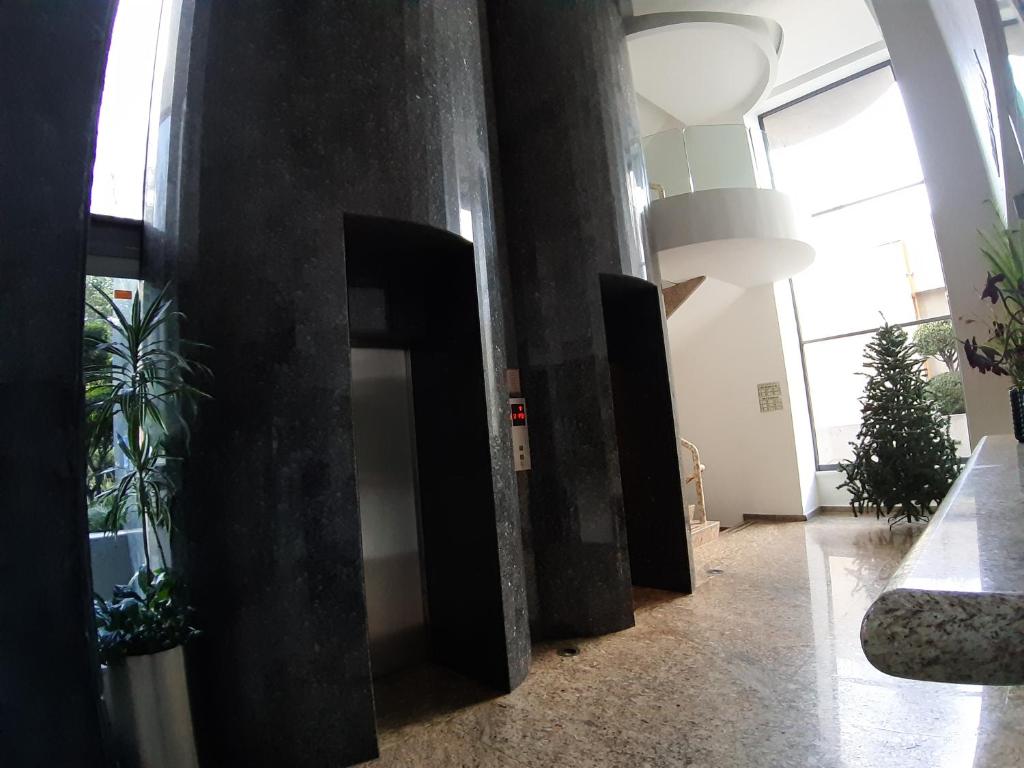 A sunlit elevator hall with dark stone columns, greenery and a curved staircase.