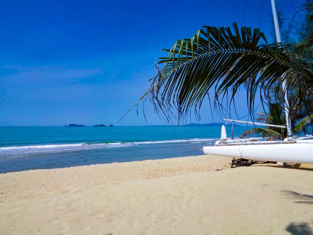 a boat sitting on a beach with a palm tree at Front Samet Beach house with swimming Pool in Rayong