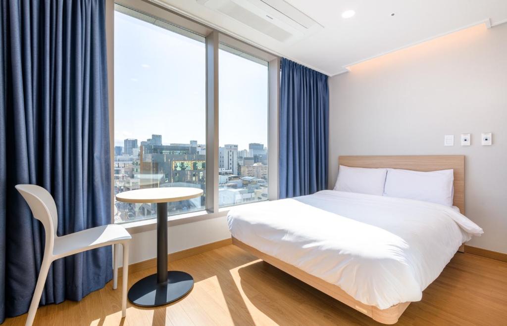 a bedroom with a bed and a table and window at Hi Residences in Jeju