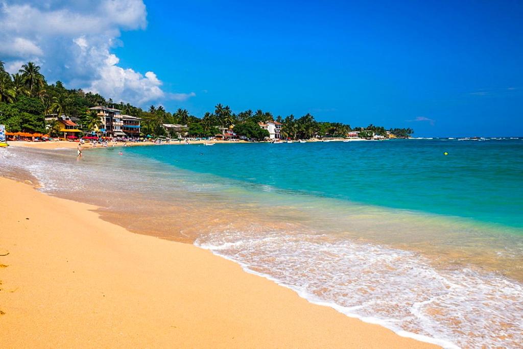 a sandy beach with the ocean and buildings in the background at Happy Night Holiday Inn in Unawatuna