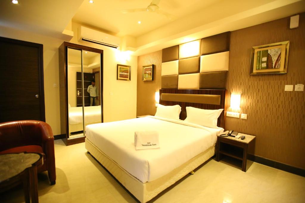 a bedroom with a large white bed and a mirror at Hotel Venition Inn in Coimbatore