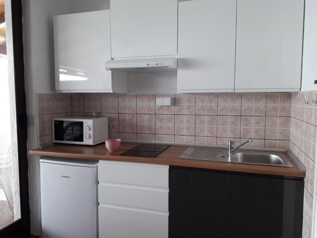 a kitchen with white cabinets and a sink and a microwave at Delfin Apartments in Sveti Juraj