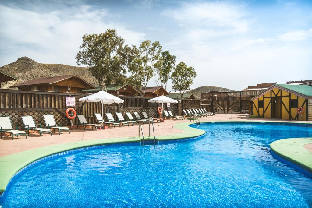 una piscina en un complejo con sillas y sombrillas en Camping Fort Bravo, en Tabernas