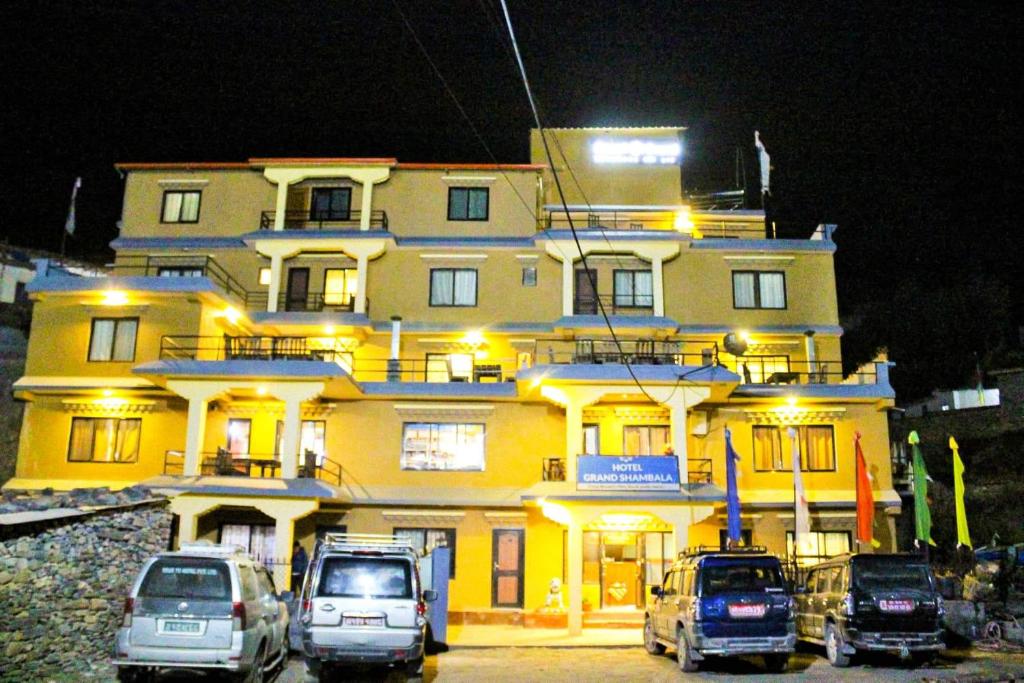a large yellow building with cars parked in front of it at Hotel Grand Shambala in Muktināth