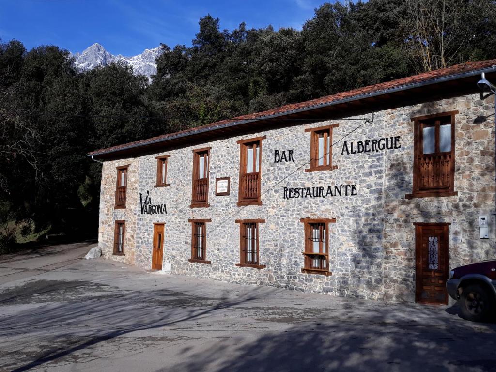 un edificio de piedra con ventanas y montañas en el fondo en Albergue La Vargona, en Camaleño