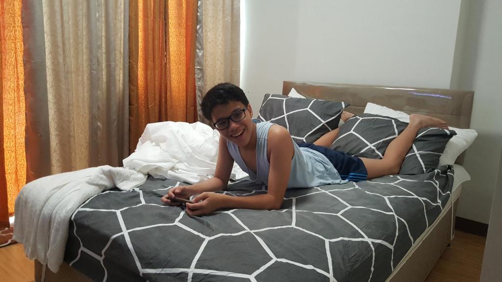 Una mujer acostada en una cama mirando su celular en Mesaverte Residences AFS Suites en Cagayán de Oro