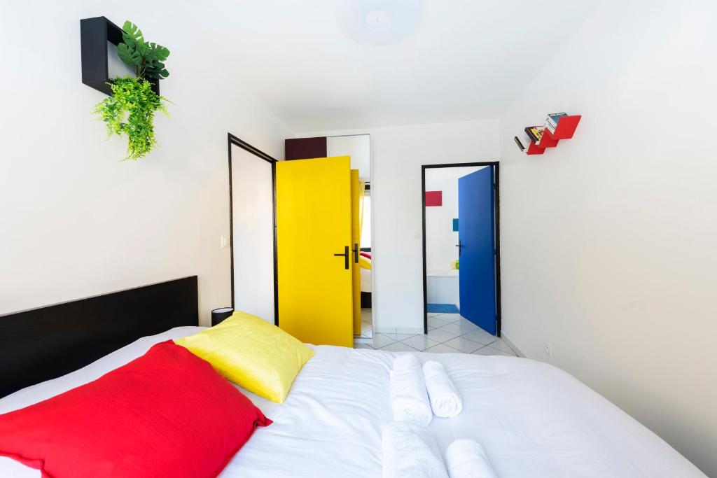 - une chambre dotée d'un lit blanc avec des oreillers rouges et jaunes dans l'établissement Appartement entier - Le mondrian - 1ch Check-in 24h, à Villeurbanne