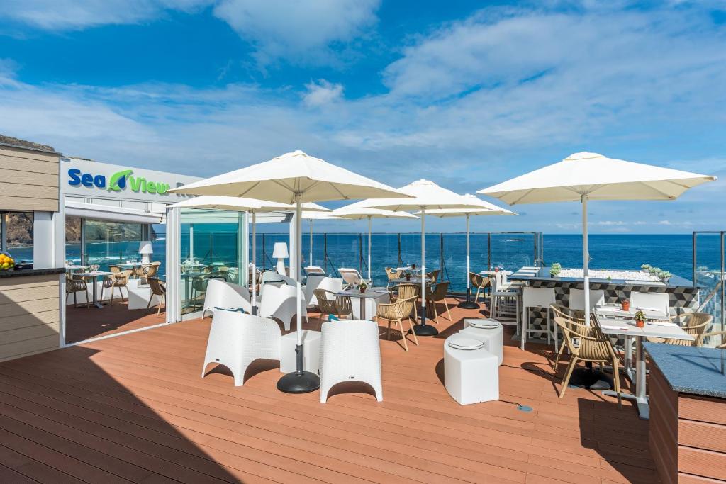 a deck with white chairs and tables and umbrellas at Aqua Natura Madeira in Porto Moniz