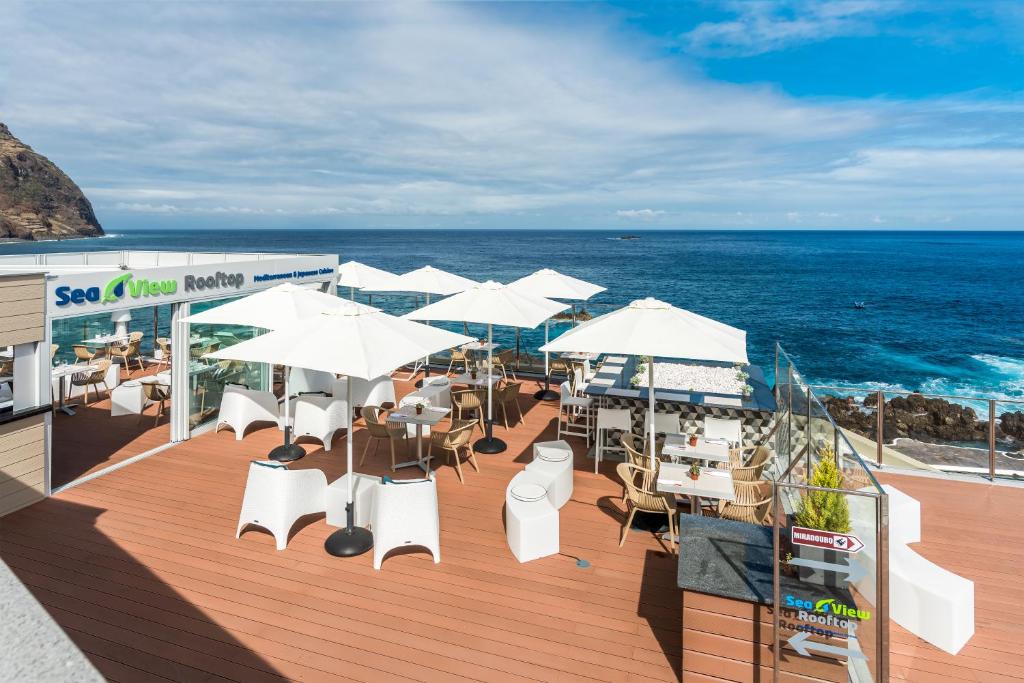a deck with tables and white umbrellas and the ocean at Aqua Natura Madeira in Porto Moniz