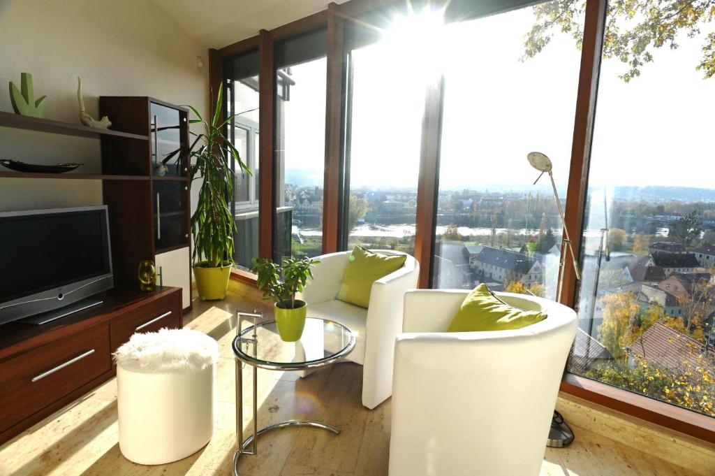 een woonkamer met witte stoelen, een tv en grote ramen bij Vogelnest in Pirna