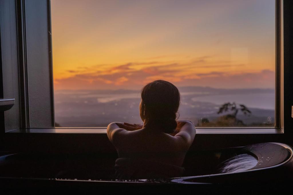 Una mujer mirando por la ventana al atardecer en ITADAKI Daisen 大山参道ホテル頂, en Daisen