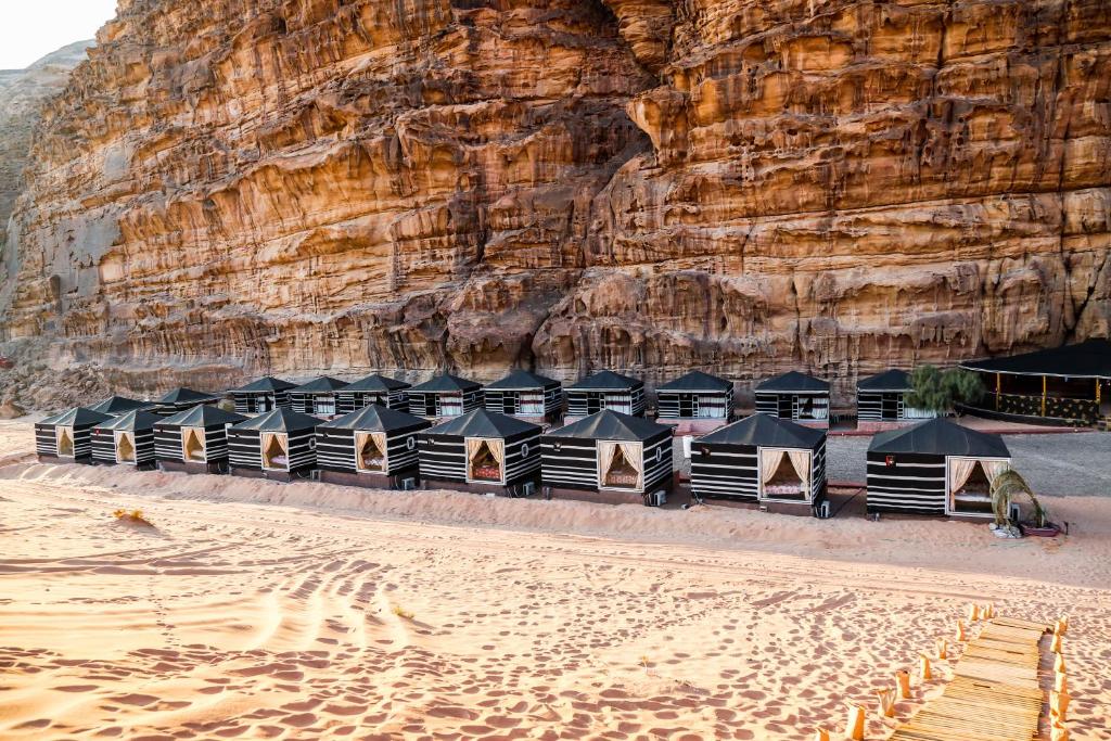 a row of tents on a beach next to a cliff at Arena Desert Camp & Adventurers in Wadi Rum