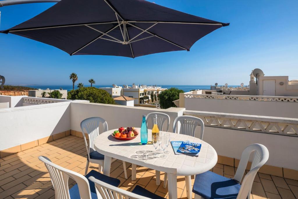 einen Tisch und Stühle auf einem Balkon mit Sonnenschirm in der Unterkunft Casa Pedrinho (Terraços de Benagil 41) in Benagil