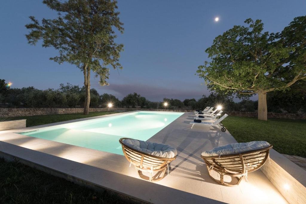 a swimming pool with chairs around it at night at Villa Althea - IsulaTravel in Modica