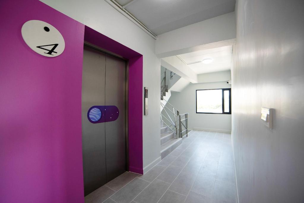 A colorful lift lobby with a magenta feature wall, patterned elevator doors and a stairwell beyond.