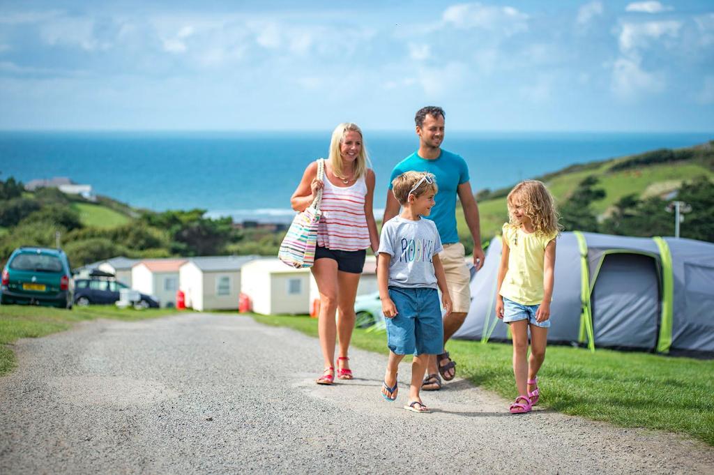 uma família a caminhar por uma estrada de cascalho com tendas em Widemouth Bay Caravan Park em Bude