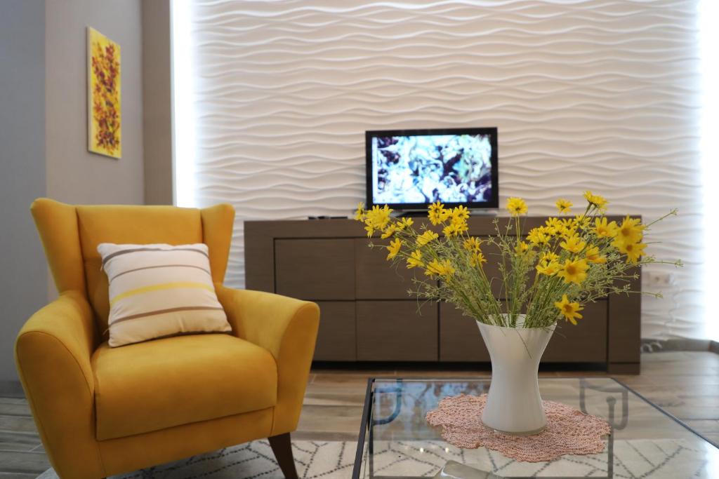 a living room with a yellow chair and a vase with yellow flowers at HD New Apartment in Tbilisi City