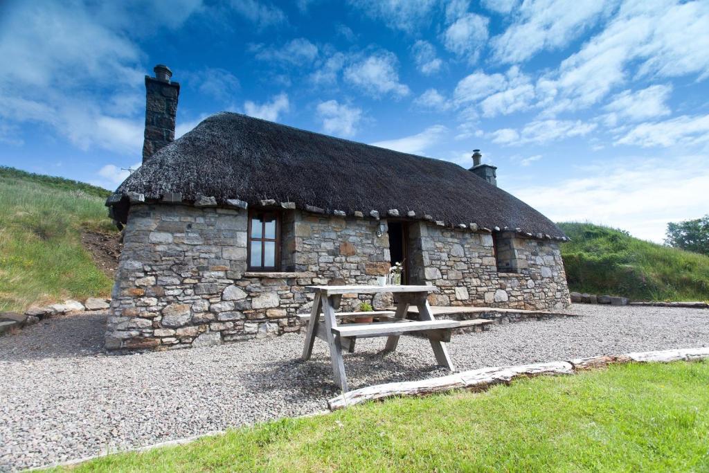 uma cabana de pedra com um banco à frente. em Tigh Phadraig at Marys Thatched Cottages em Elgol