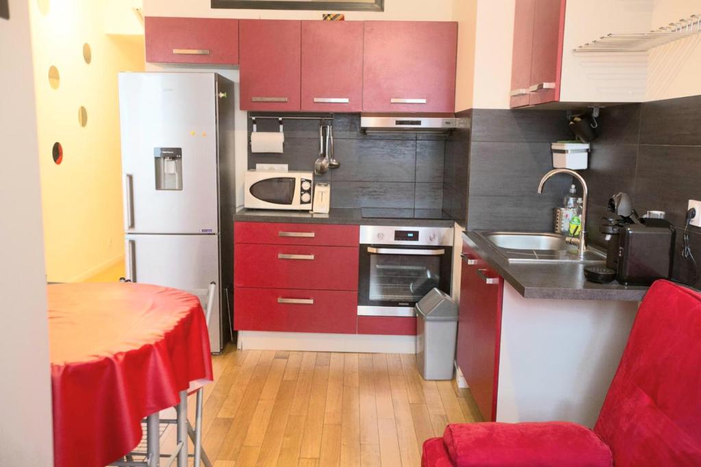 a kitchen with red cabinets and a table and a refrigerator at Location F3 Fontenay-Aux-Roses in Fontenay-aux-Roses