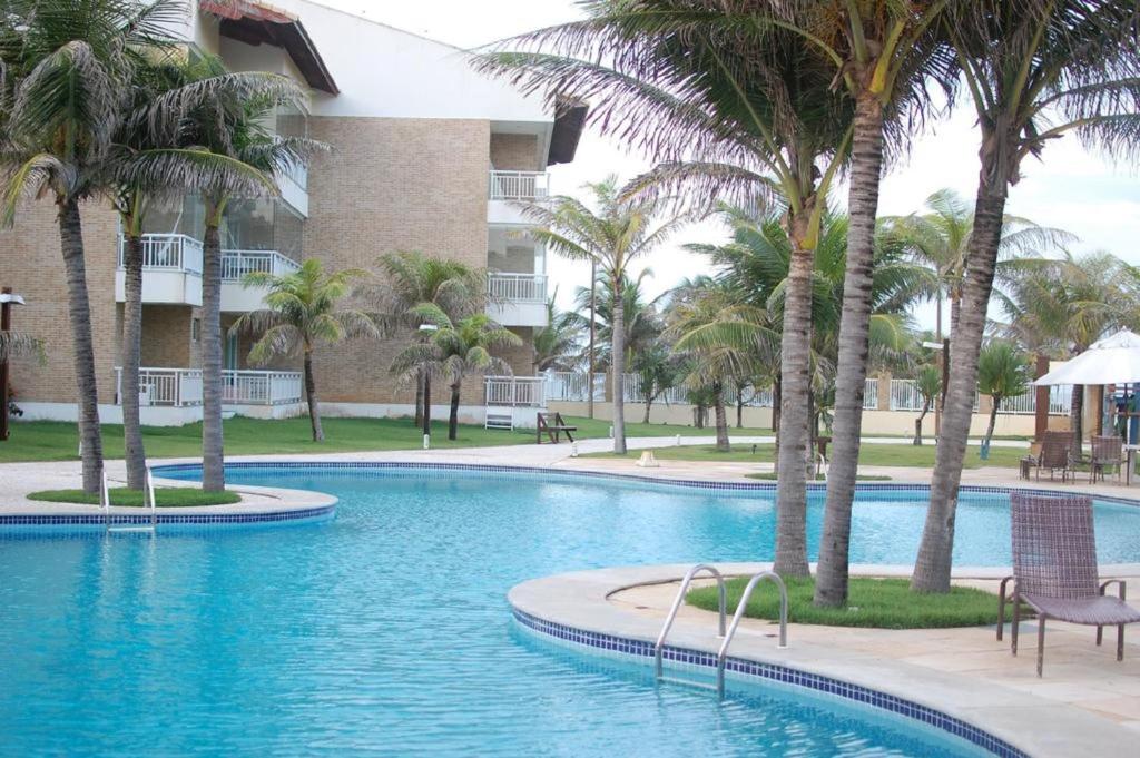 una piscina con palmeras frente a un edificio en Apartamento Pé na Areia Porto das Dunas - Paraiso das Dunas, en Aquiraz