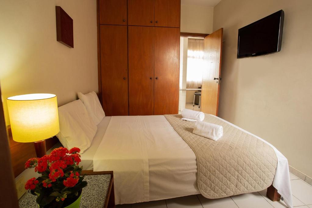 a bedroom with a white bed with a lamp and flowers at Pampulha Flat in Belo Horizonte