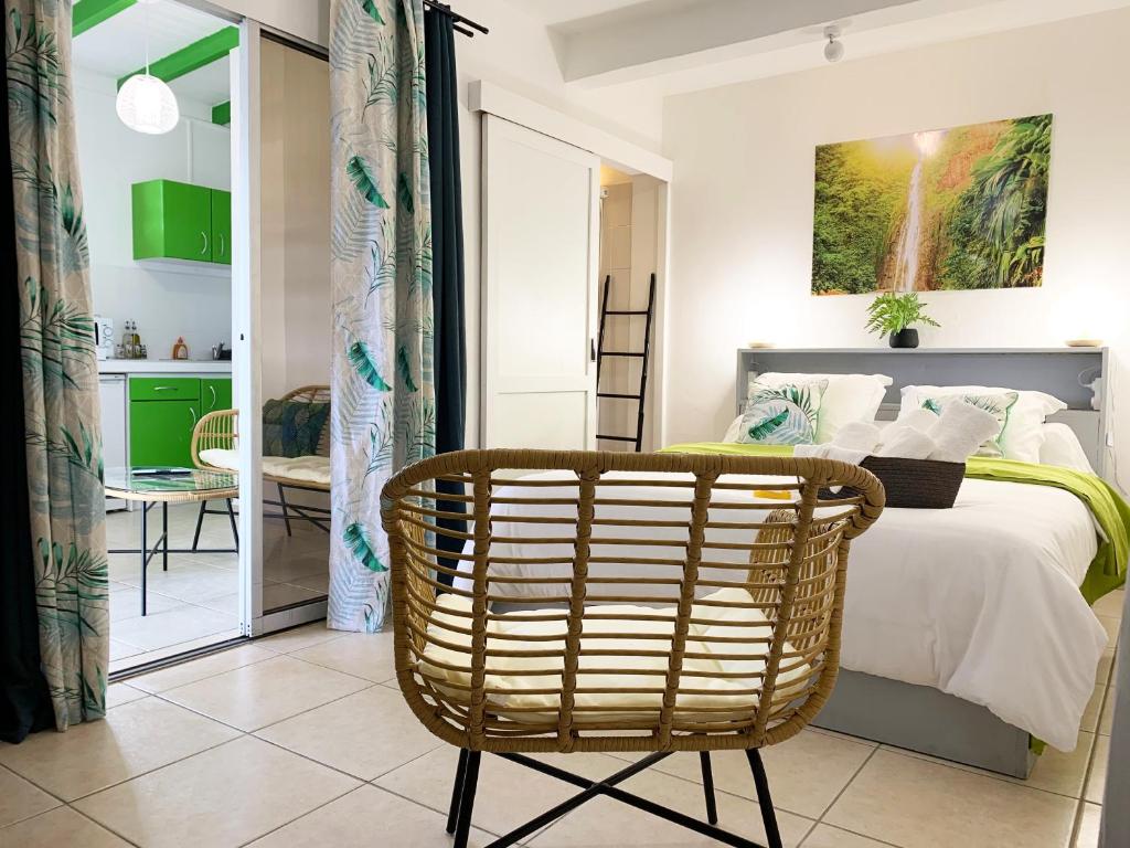 a bedroom with a bed and a rattan chair at Le ZANDOLI (Appartement avec vue) in Petit-Bourg