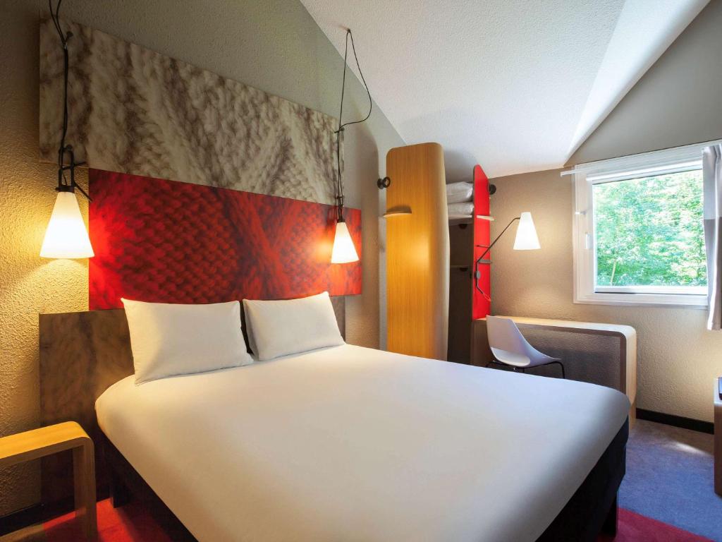 a bedroom with a large white bed with a red headboard at ibis Velizy Jouy-En-Josas in Jouy-en-Josas