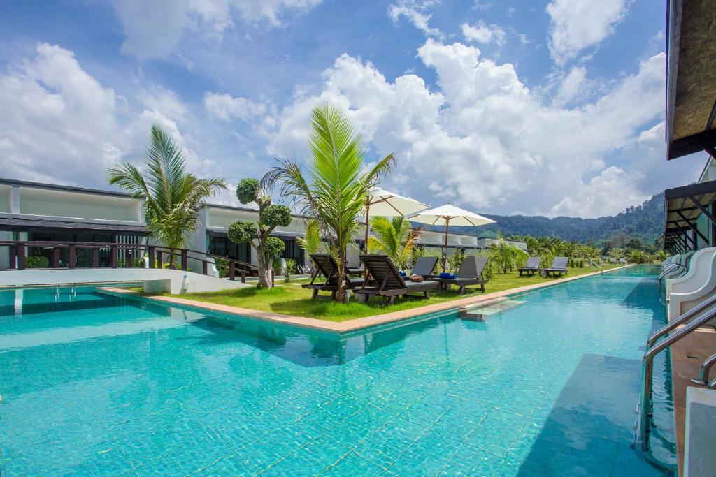 a large swimming pool with chairs and trees next to a building at The La Valle'e Resort in Khao Lak