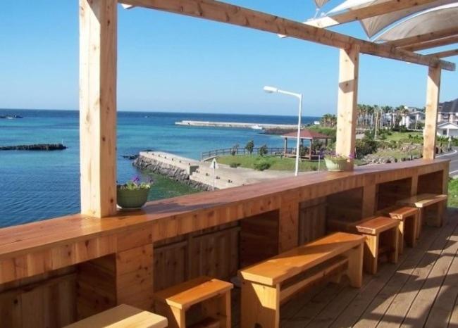 una terraza de madera con bancos y vistas al océano. en Africa Guesthouse en Jeju