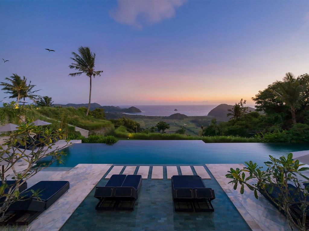 a resort pool with chairs and a sunset at Selong Selo Resort and Residences in Selong Belanak