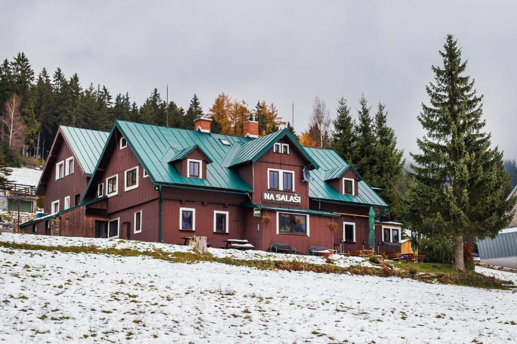 ein großes Haus mit grünem Dach im Schnee in der Unterkunft Apartmany Na Salasi in Pec pod Sněžkou