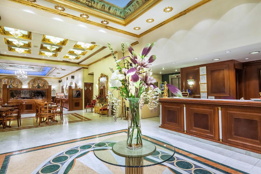 a vase of flowers on a glass table in a lobby at Imperial Palace Classical Hotel Thessaloniki in Thessaloniki