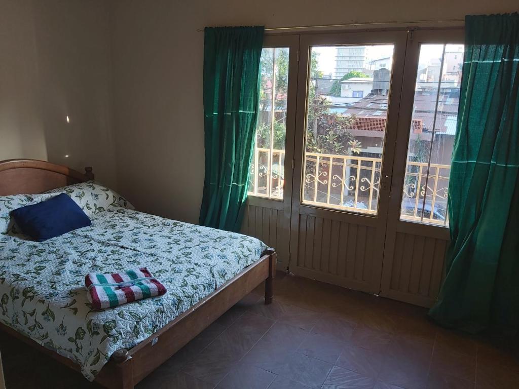 een slaapkamer met een bed en een balkon met groene gordijnen bij Habitaciones Villa Blosset in Posadas
