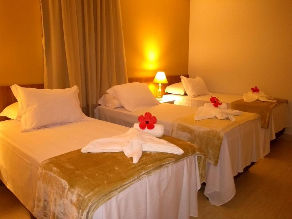 three beds in a hotel room with red flowers on them at Pousada Aconchego Noronha in Fernando de Noronha
