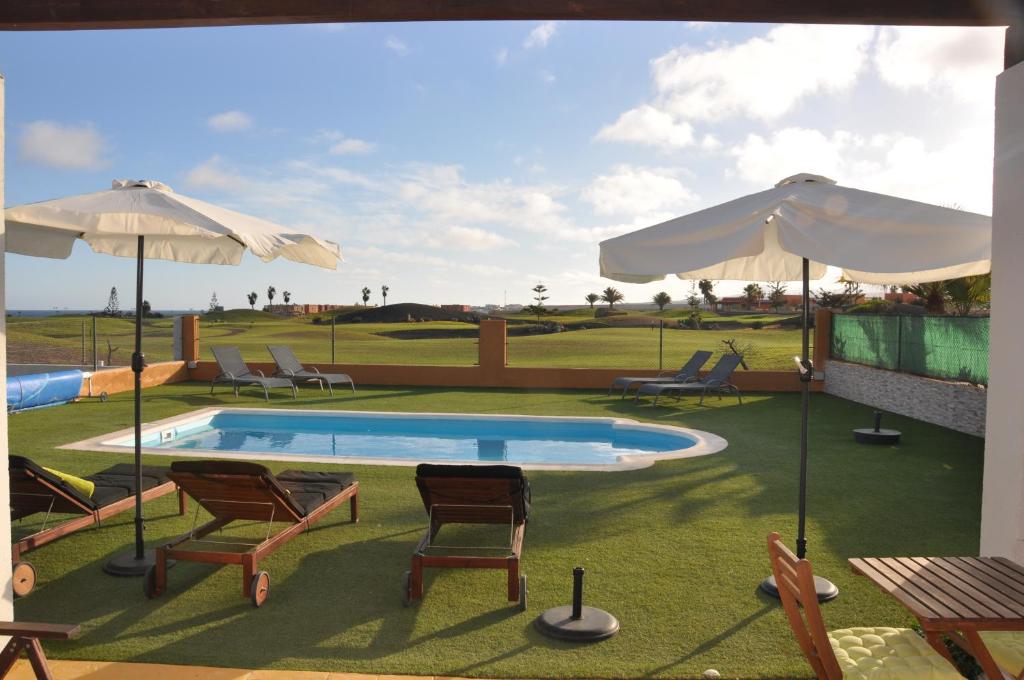 a swimming pool with chairs and umbrellas on a yard at Villa Surprise only Solar Energy in Caleta De Fuste