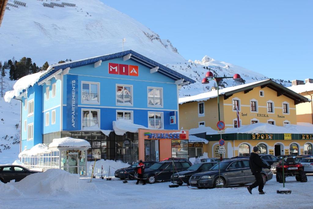 un bâtiment bleu avec des voitures garées dans la neige dans l'établissement MIA Appartements - non-serviced Appartements, à Obertauern