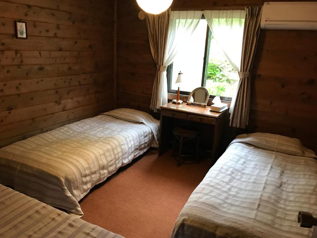 a bedroom with two beds and a desk and a window at Pension Sanrinsha in Shizukuishi