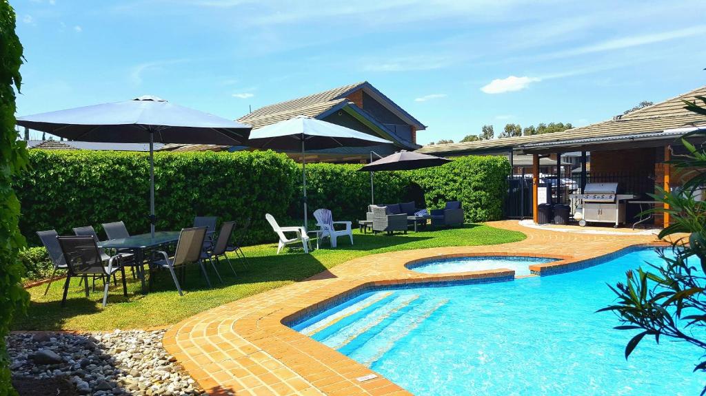 uma piscina num quintal com cadeiras e guarda-sóis em The Heritage Bendigo em Bendigo