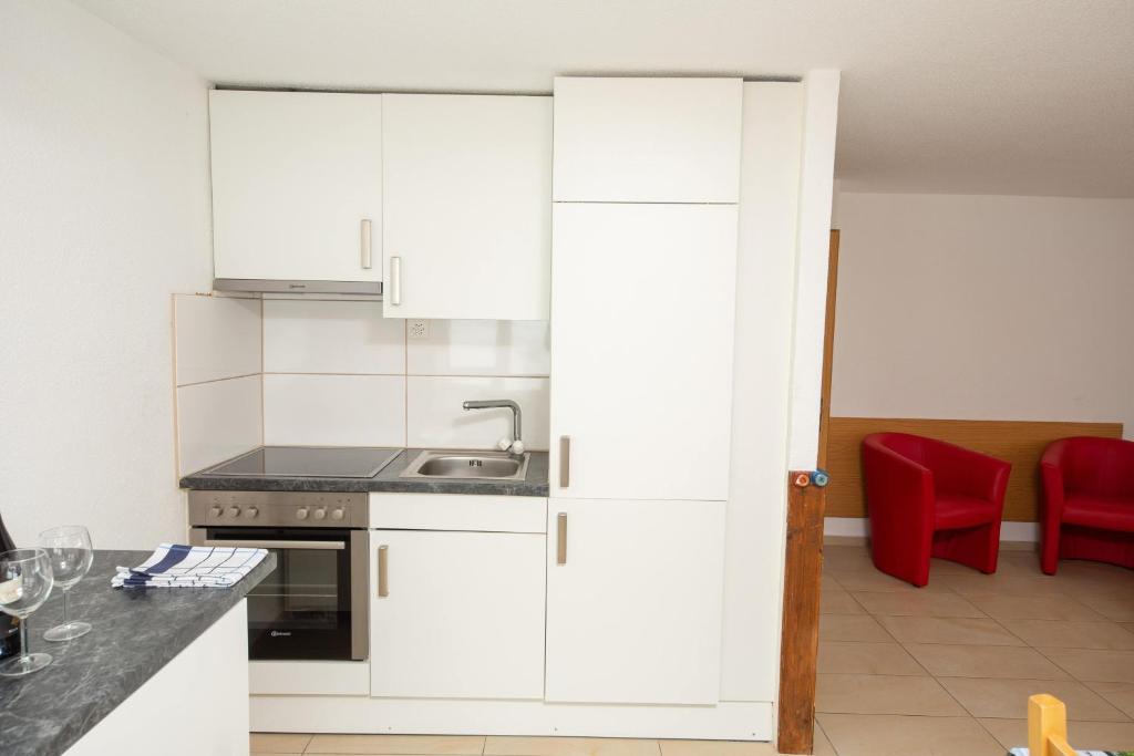 a kitchen with white cabinets and a red chair at Haus Alfa in Saas-Fee
