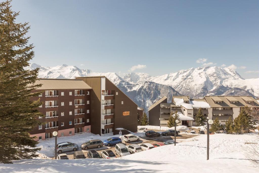 un hôtel avec des voitures garées dans un parking avec des montagnes enneigées dans l'établissement Residence Les Horizons d'Huez - maeva Home, à L'Alpe-d'Huez
