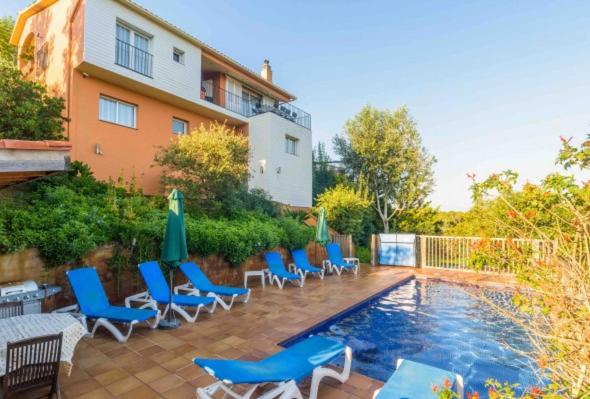 uma piscina com cadeiras e guarda-sóis ao lado de um edifício em Villa Los Robles em Begur