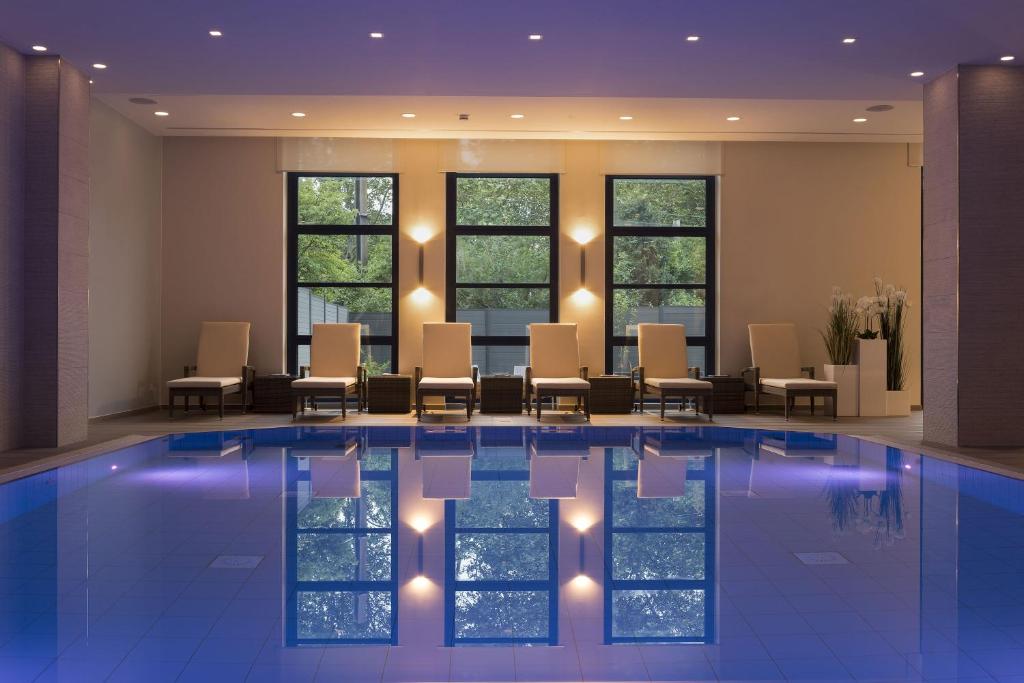 a hotel lobby with a pool with chairs and windows at Maritim Hotel Bonn in Bonn