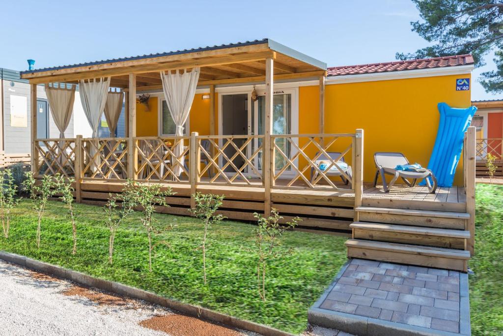 ein kleines gelbes Haus mit einer Terrasse und einem blauen Stuhl in der Unterkunft Camping Adria Mobile Homes Lanterna in Poreč